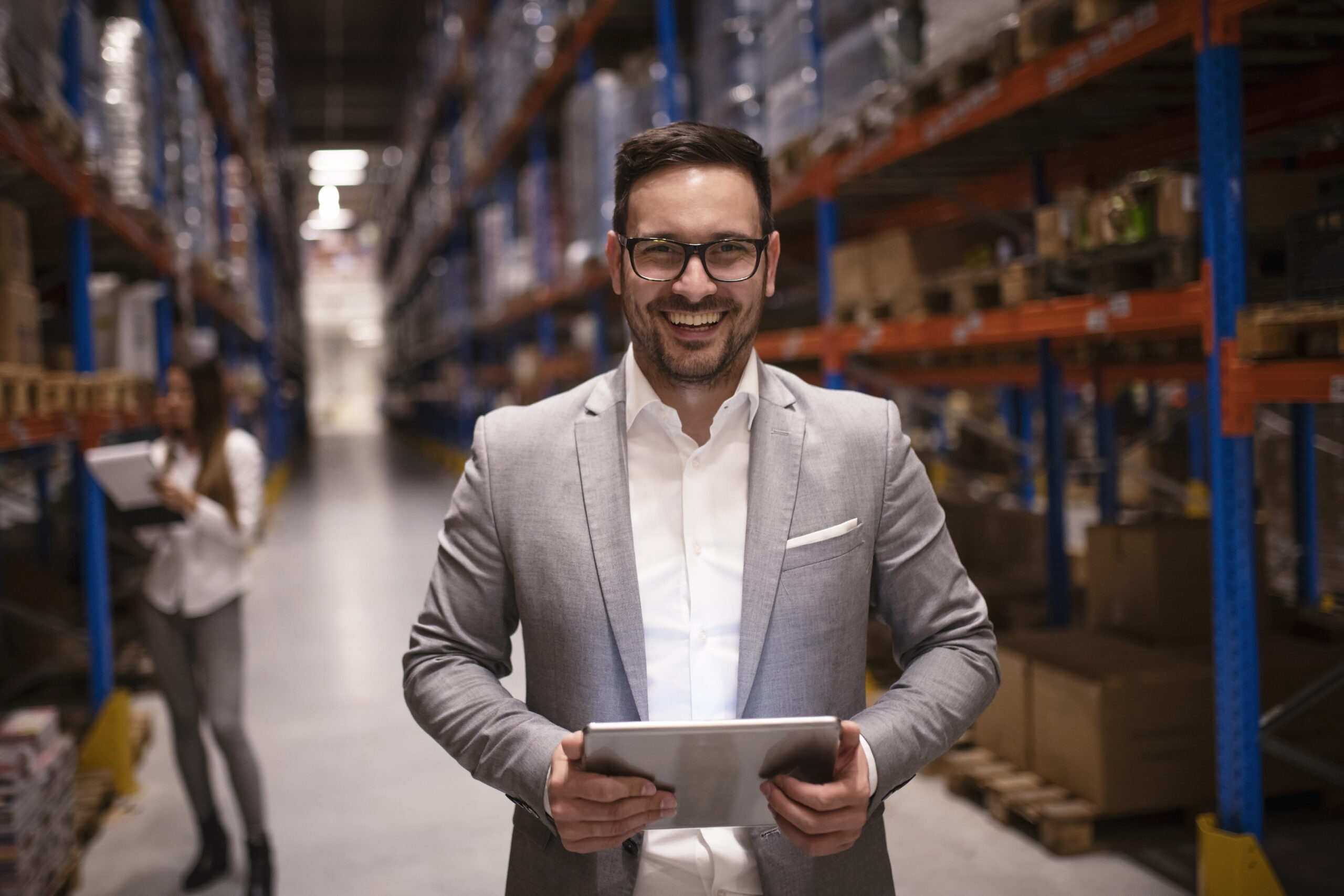 Cheerful and successful middle aged caucasian manager businessman holding tablet computer in large warehouse organizing distribution.